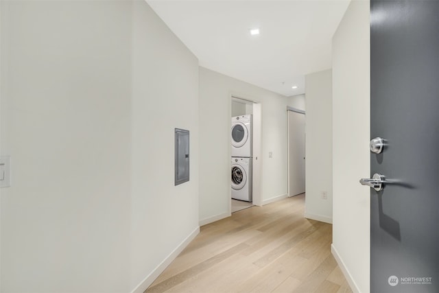 hallway featuring electric panel, stacked washer and dryer, and light hardwood / wood-style floors