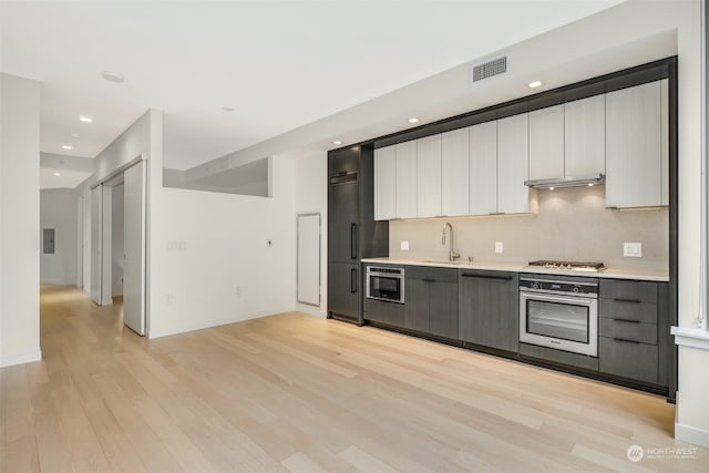 kitchen with appliances with stainless steel finishes, tasteful backsplash, sink, light hardwood / wood-style flooring, and white cabinetry