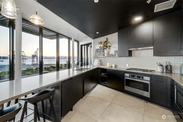 kitchen with sink, stainless steel appliances, backsplash, decorative light fixtures, and light tile patterned floors