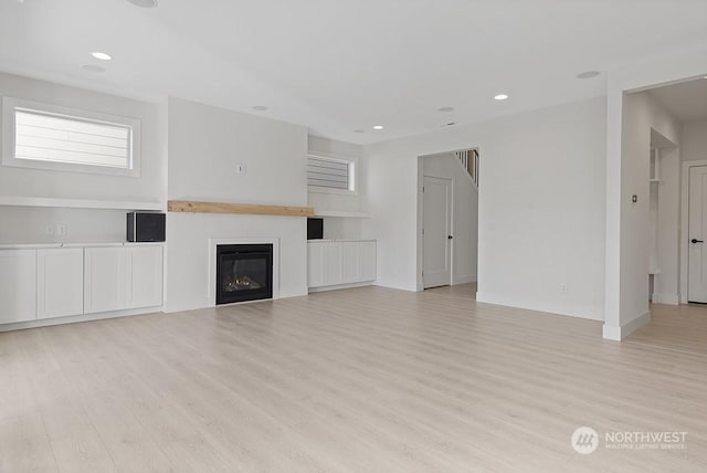 unfurnished living room with built in shelves and light hardwood / wood-style floors