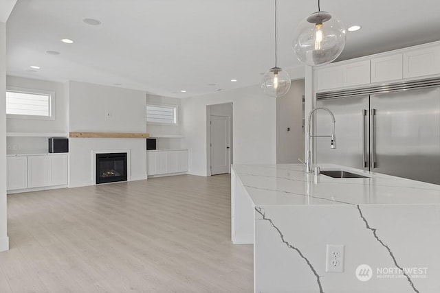 kitchen with light stone countertops, sink, white cabinetry, hanging light fixtures, and built in fridge