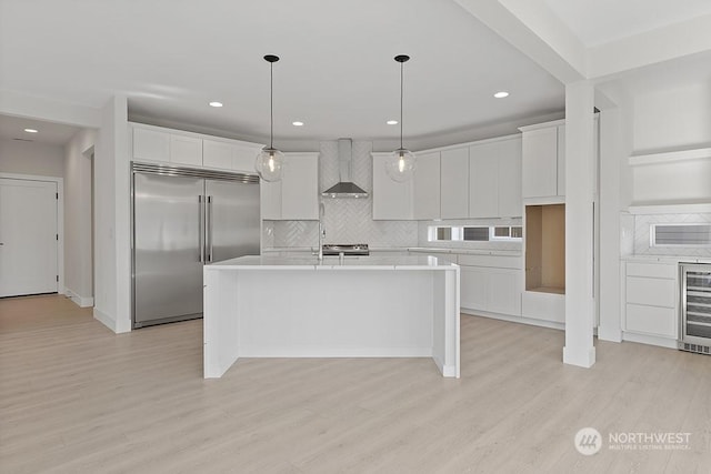 kitchen featuring white cabinets, appliances with stainless steel finishes, hanging light fixtures, and wall chimney range hood