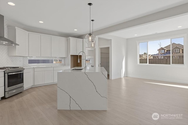 kitchen featuring decorative backsplash, stainless steel gas stove, white cabinetry, hanging light fixtures, and an island with sink