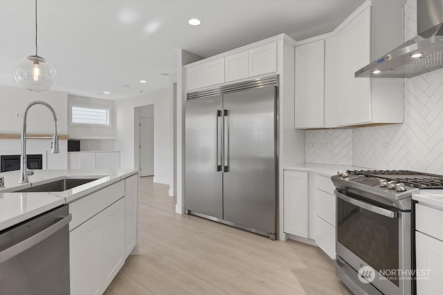 kitchen with sink, wall chimney exhaust hood, decorative backsplash, white cabinets, and appliances with stainless steel finishes