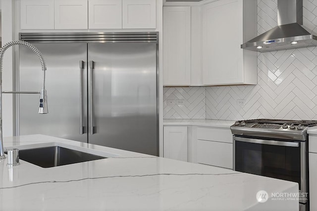 kitchen featuring white cabinetry, light stone countertops, wall chimney exhaust hood, and stainless steel appliances