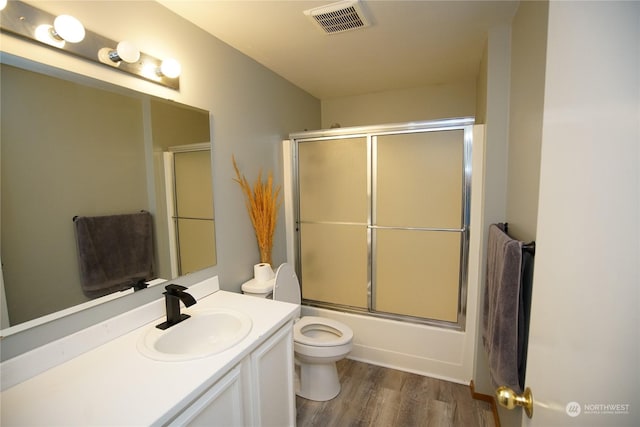 full bathroom with shower / bath combination with glass door, hardwood / wood-style floors, vanity, and toilet