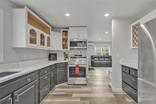 kitchen with gray cabinetry, white cabinetry, light stone countertops, appliances with stainless steel finishes, and light wood-type flooring