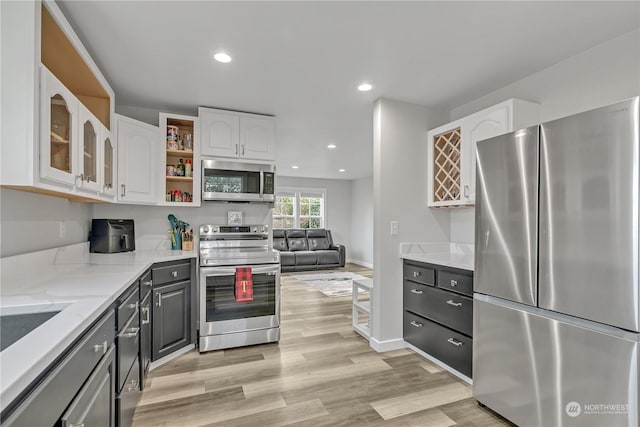 kitchen with light stone countertops, stainless steel appliances, white cabinetry, and light hardwood / wood-style floors