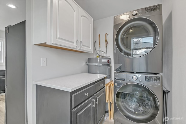 clothes washing area featuring cabinets, strapped water heater, and stacked washing maching and dryer