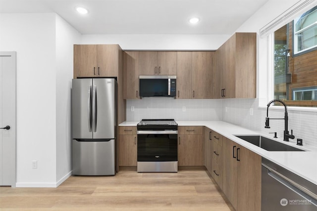 kitchen with appliances with stainless steel finishes, tasteful backsplash, light hardwood / wood-style flooring, and sink