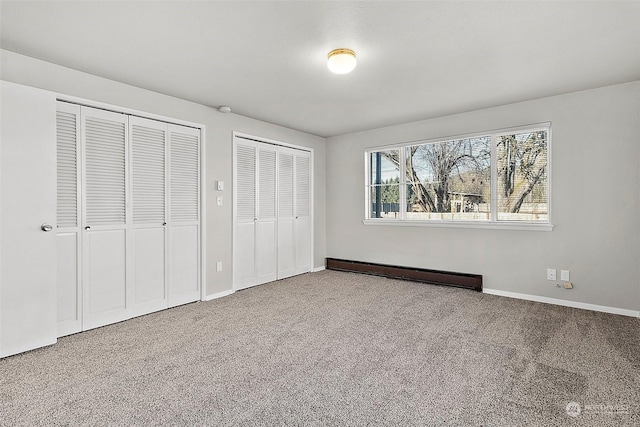 unfurnished bedroom with carpet floors, two closets, and a baseboard heating unit