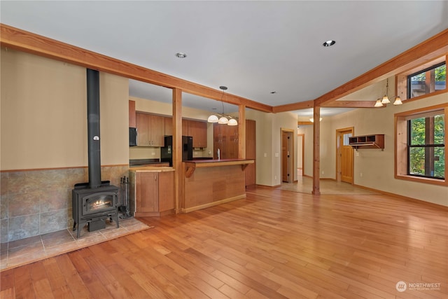 unfurnished living room featuring light wood-type flooring, a wood stove, and a chandelier