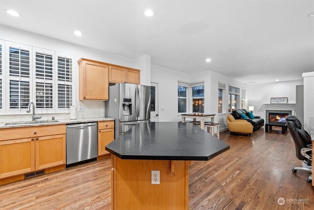 kitchen featuring sink, tasteful backsplash, a center island, light wood-type flooring, and stainless steel appliances