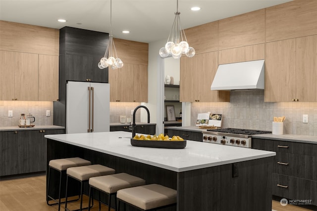 kitchen featuring custom exhaust hood, high end white fridge, a kitchen island with sink, and decorative light fixtures