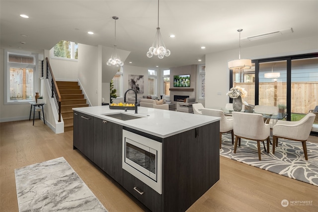 kitchen with stainless steel microwave, an inviting chandelier, sink, hanging light fixtures, and an island with sink