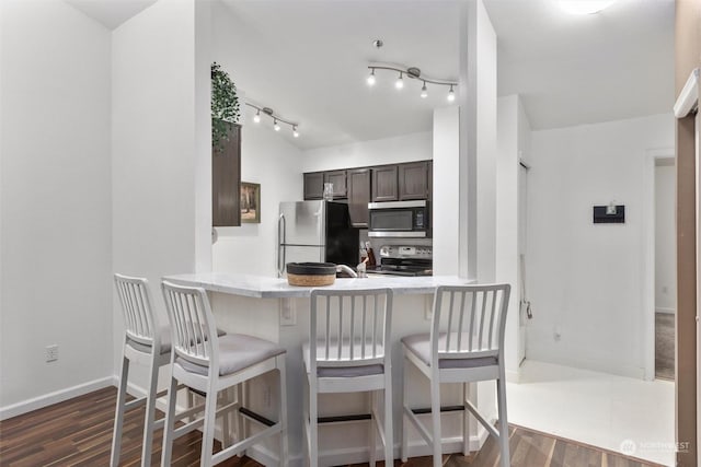 kitchen with a kitchen breakfast bar, appliances with stainless steel finishes, kitchen peninsula, dark hardwood / wood-style floors, and dark brown cabinets