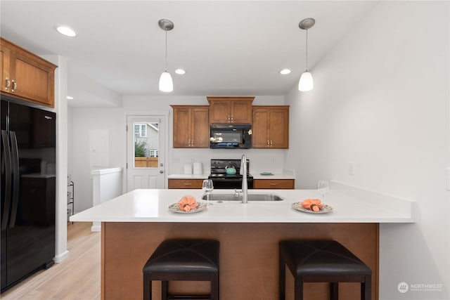 kitchen with a kitchen breakfast bar, light wood-type flooring, sink, black appliances, and hanging light fixtures