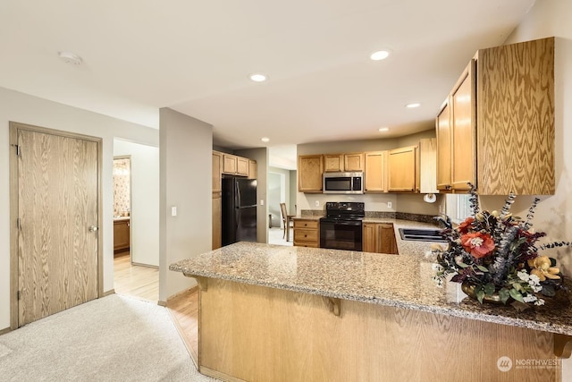 kitchen featuring black appliances, light stone countertops, kitchen peninsula, light brown cabinetry, and sink