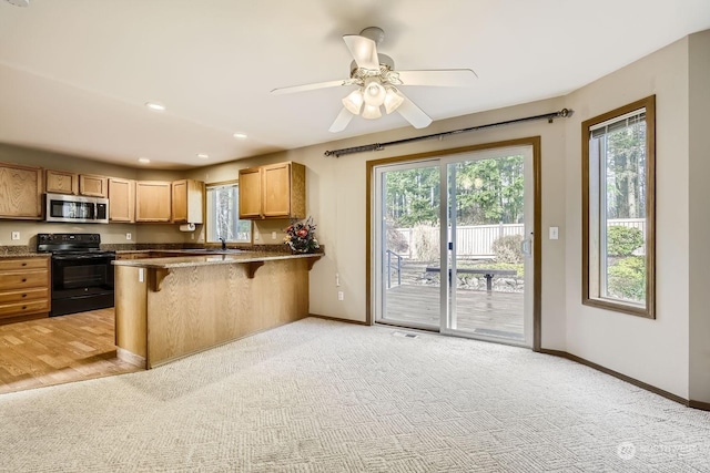 kitchen featuring light carpet, black range with electric stovetop, kitchen peninsula, ceiling fan, and a breakfast bar