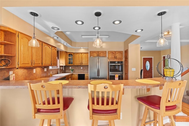 kitchen with kitchen peninsula, stainless steel appliances, decorative backsplash, a kitchen breakfast bar, and sink