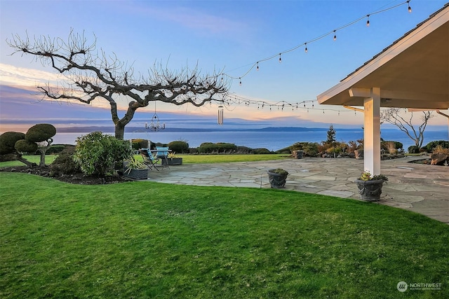 yard at dusk with a patio area and a water view