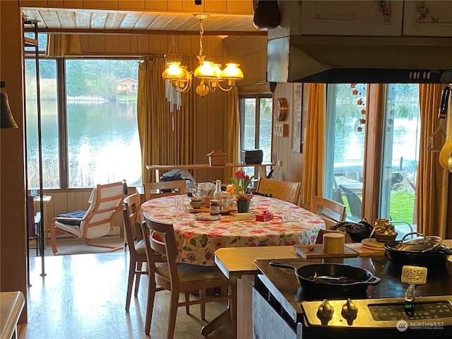 dining space featuring a water view, a chandelier, wooden walls, and wooden ceiling