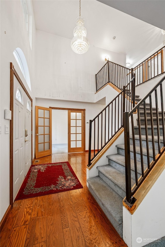 entrance foyer with a chandelier, french doors, a towering ceiling, and wood-type flooring