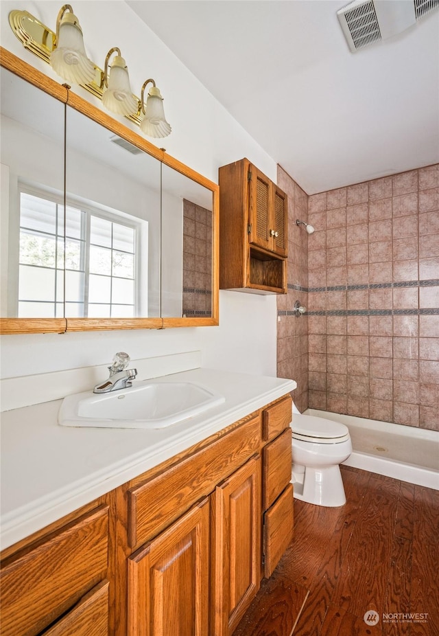 bathroom featuring hardwood / wood-style floors, vanity, a tile shower, and toilet