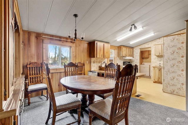 carpeted dining room featuring a notable chandelier, washer and clothes dryer, lofted ceiling, and wood walls