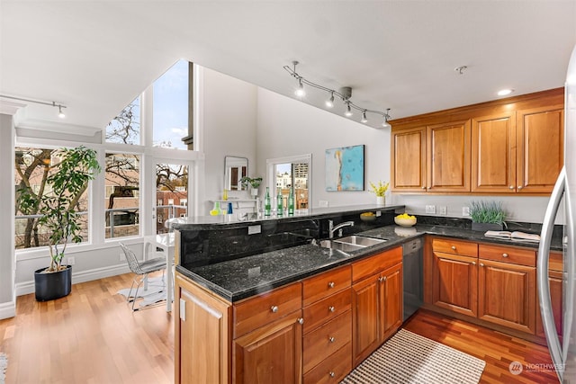 kitchen featuring sink, light hardwood / wood-style flooring, dark stone countertops, appliances with stainless steel finishes, and kitchen peninsula