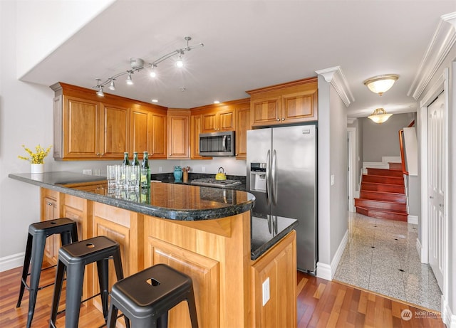 kitchen with dark stone counters, a kitchen breakfast bar, crown molding, kitchen peninsula, and stainless steel appliances