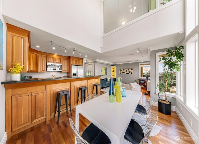 kitchen featuring a high ceiling, a kitchen breakfast bar, dark hardwood / wood-style flooring, crown molding, and appliances with stainless steel finishes