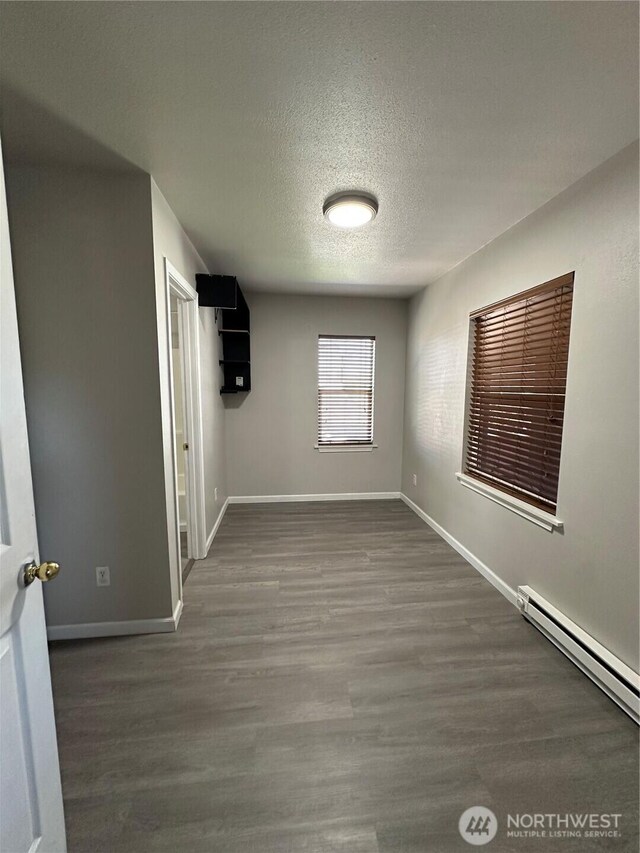 empty room with wood finished floors, baseboards, a textured ceiling, and a baseboard radiator