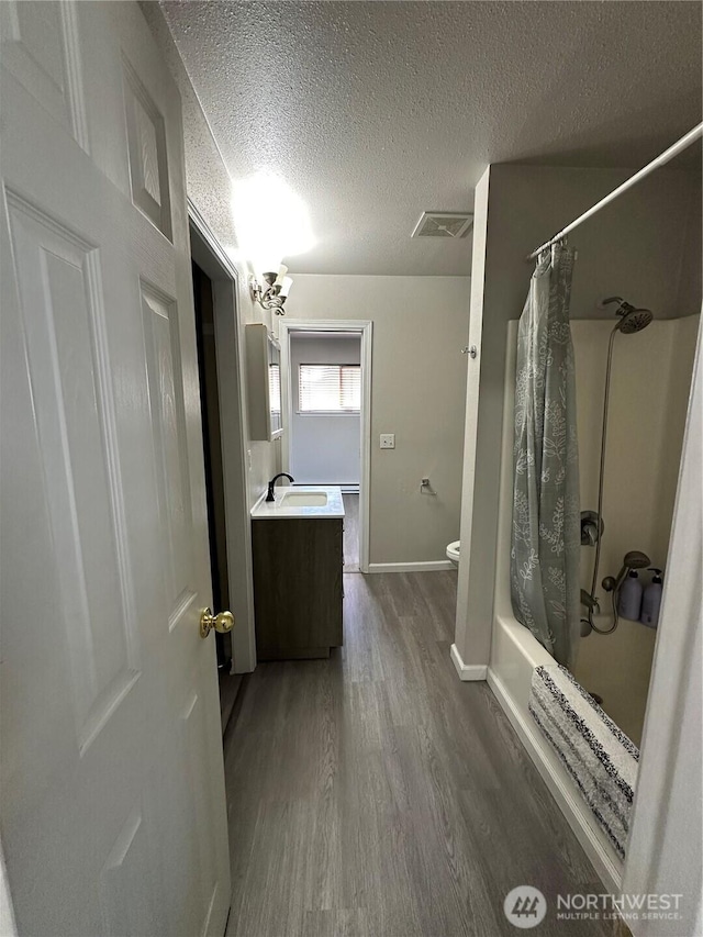 full bath featuring wood finished floors, a textured ceiling, vanity, shower / bath combination with curtain, and baseboards