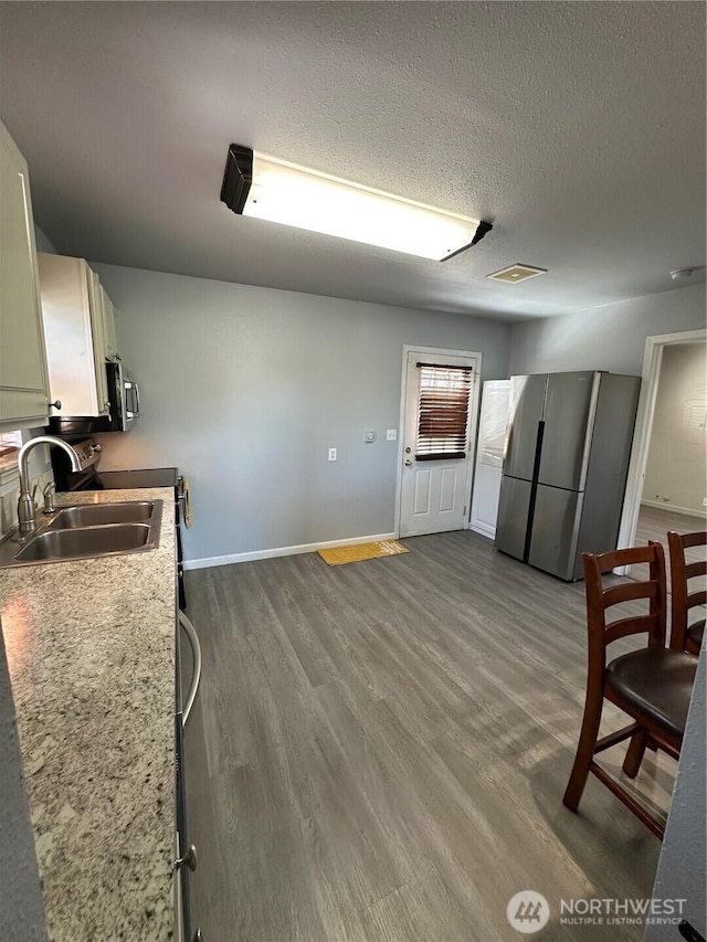 kitchen with light countertops, a sink, dark wood-type flooring, baseboards, and appliances with stainless steel finishes