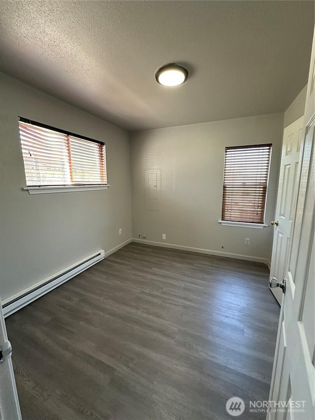 unfurnished bedroom featuring a baseboard heating unit, dark wood finished floors, baseboards, and a textured ceiling