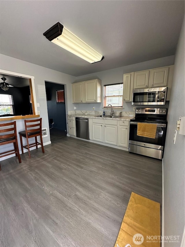 kitchen with dark wood finished floors, baseboards, stainless steel appliances, and a sink