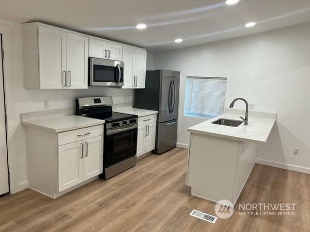 kitchen with sink, appliances with stainless steel finishes, light hardwood / wood-style floors, white cabinets, and kitchen peninsula