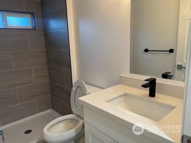 bathroom with vanity, toilet, and a tile shower