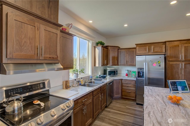 kitchen with sink, hardwood / wood-style flooring, appliances with stainless steel finishes, extractor fan, and light stone countertops