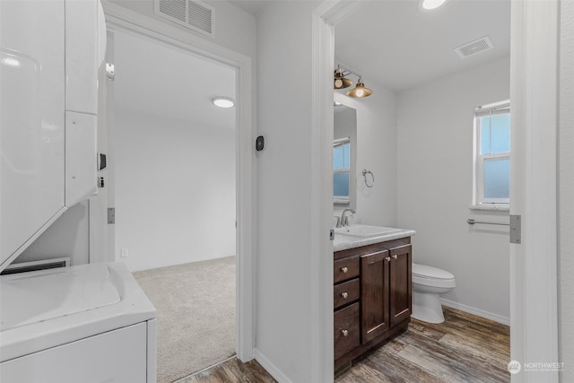 bathroom featuring hardwood / wood-style floors, vanity, stacked washer and dryer, and toilet