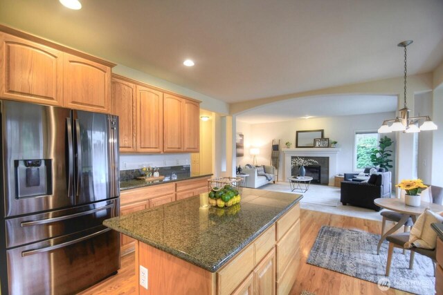 kitchen featuring light wood-style flooring, a fireplace, a kitchen island, refrigerator with ice dispenser, and open floor plan