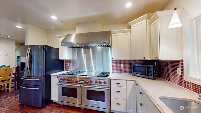 kitchen with decorative backsplash, stainless steel appliances, sink, wall chimney range hood, and pendant lighting