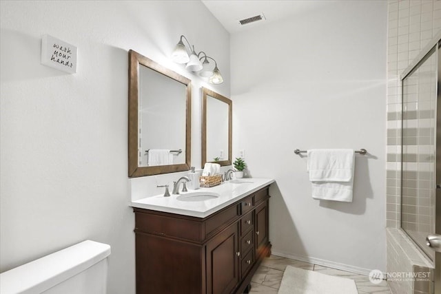 bathroom featuring toilet, vanity, and a shower with shower door