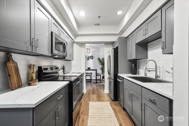 kitchen with light stone counters, decorative backsplash, light wood-type flooring, appliances with stainless steel finishes, and sink