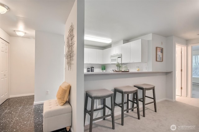 kitchen featuring light countertops, white microwave, a peninsula, and white cabinetry