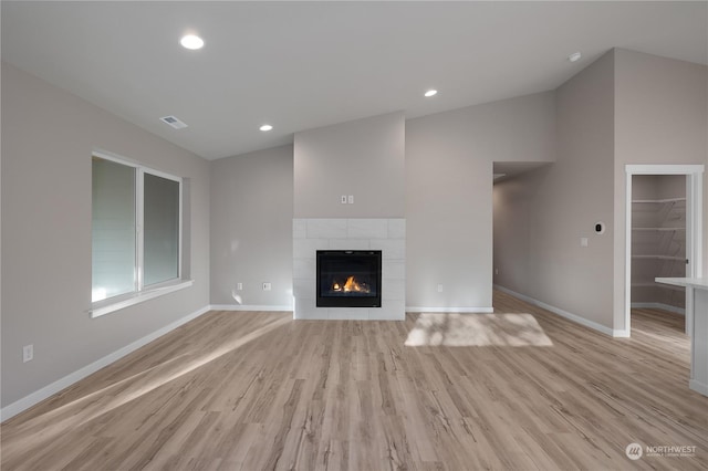 unfurnished living room with lofted ceiling, light wood-type flooring, and a tile fireplace