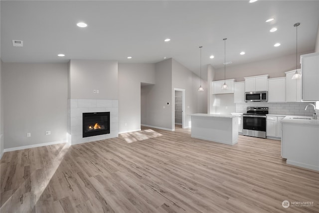 kitchen featuring white cabinets, hanging light fixtures, a fireplace, appliances with stainless steel finishes, and a kitchen island