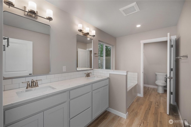 bathroom with a tub to relax in, tasteful backsplash, vanity, hardwood / wood-style floors, and toilet