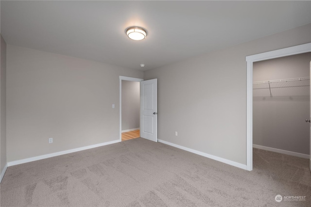 unfurnished bedroom with a walk in closet, a closet, and light colored carpet